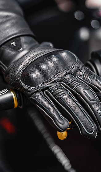Close-up of a black leather glove on a hand gripping a motorcycle handlebar.