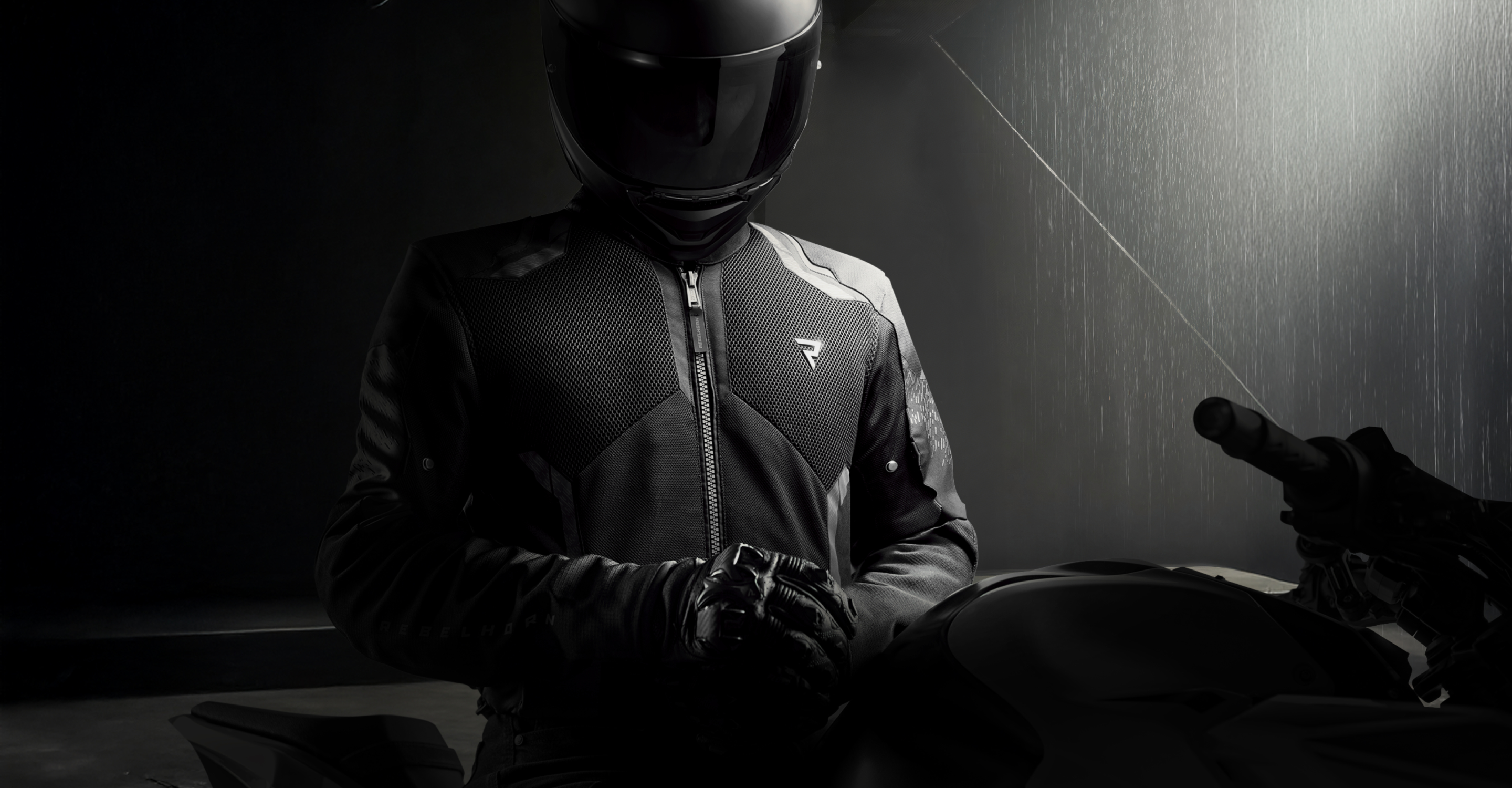 Person wearing a black motorcycle helmet and jacket in a dimly lit room.
