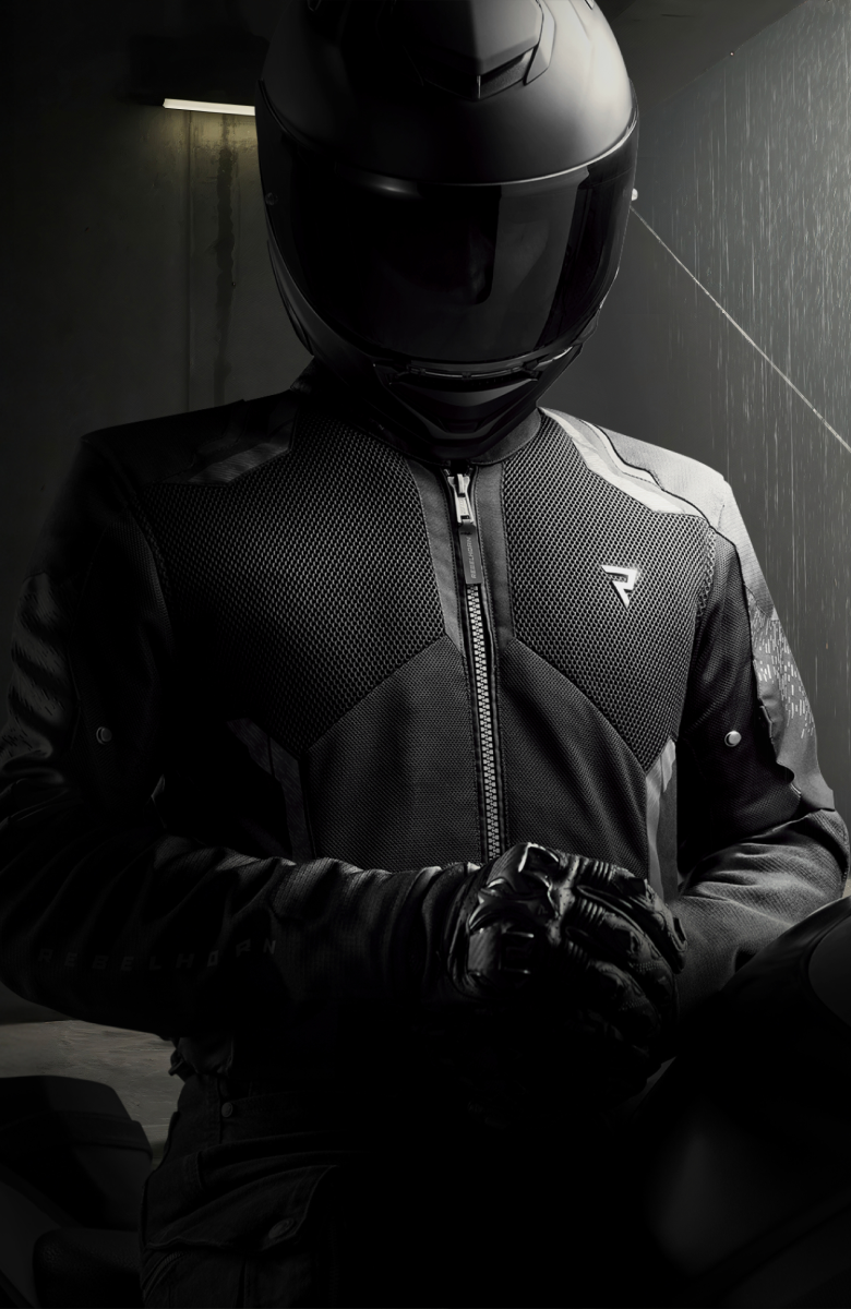 Person wearing a black motorcycle helmet and jacket in a dimly lit room.