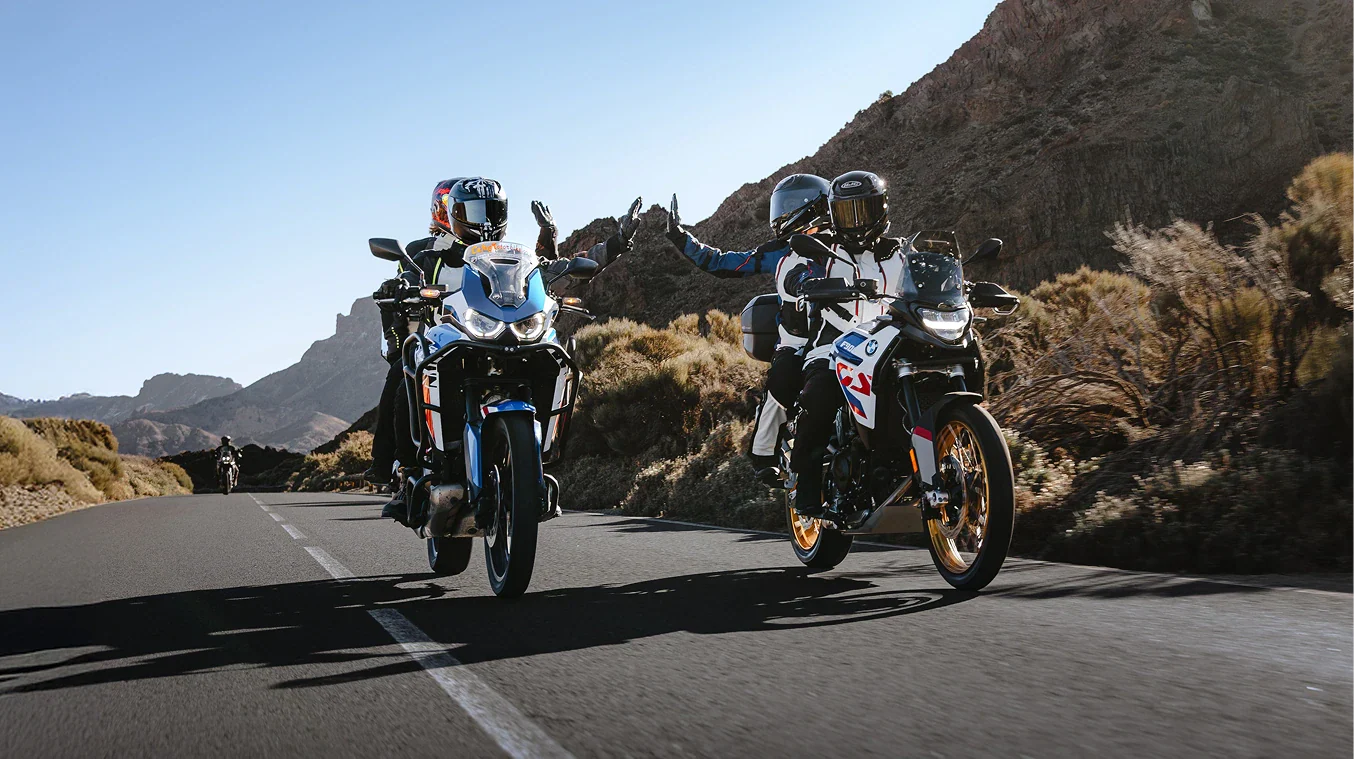 Two motorcyclists on a desert road with mountains in the background