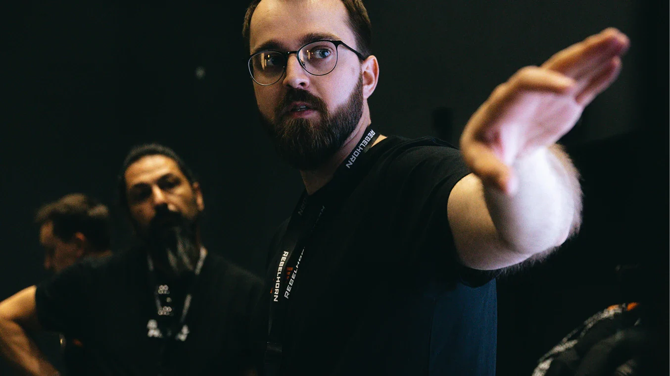 Man with glasses and beard pointing forward with a dark background
